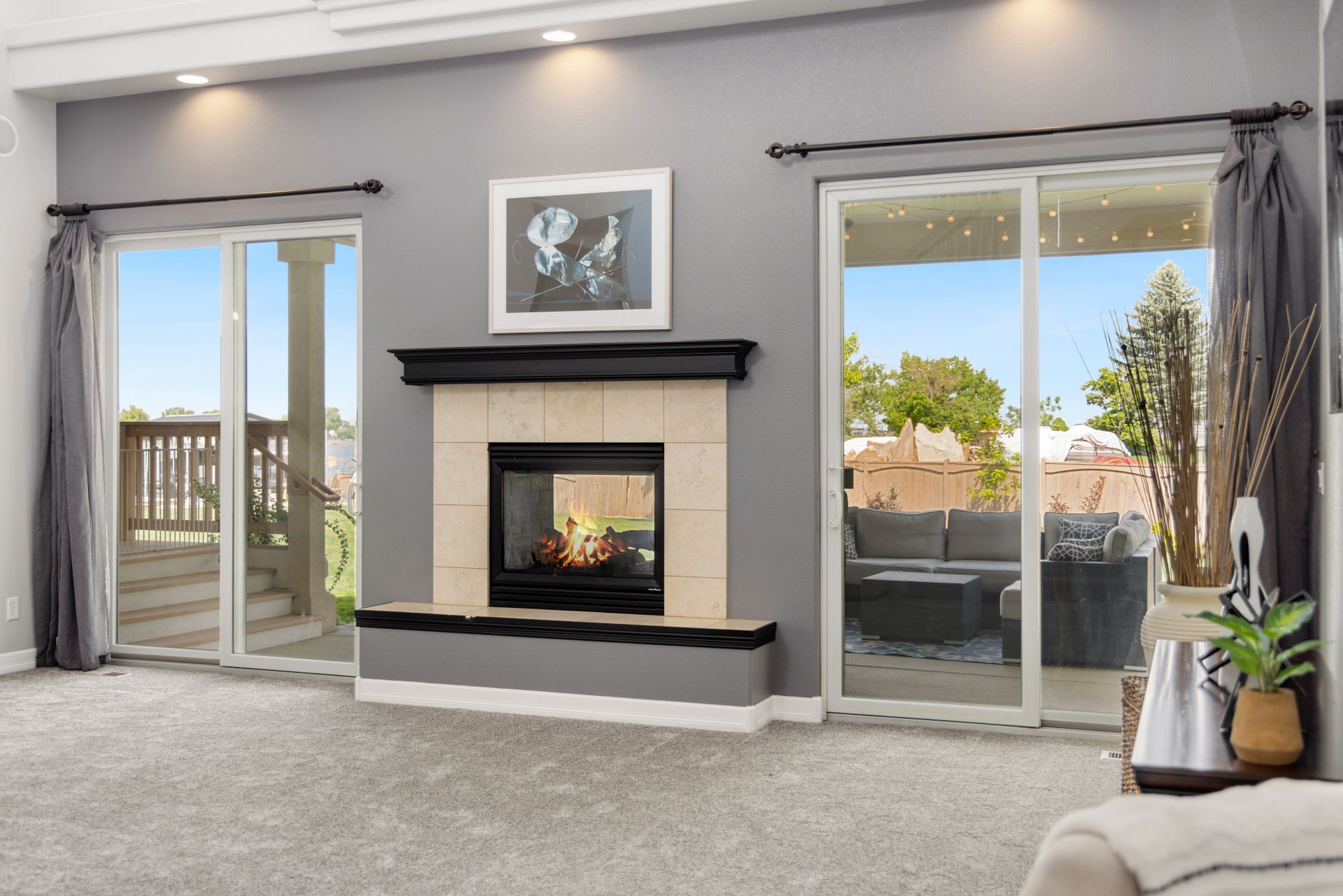 Two white vinyl sliding glass patio doors with gray drapes on either side of a see-through fireplace