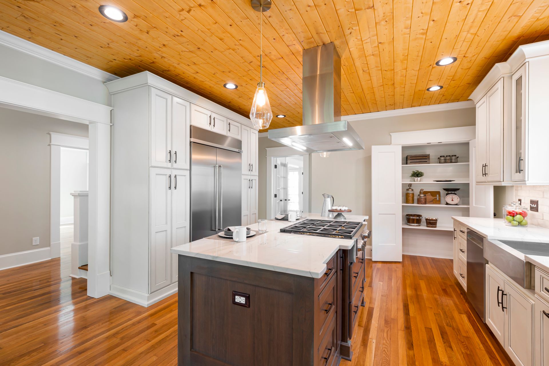 Pair of white paneled doors open on a walk-in pantry with deep white shelves holding glass canisters and baskets, off a white kitchen