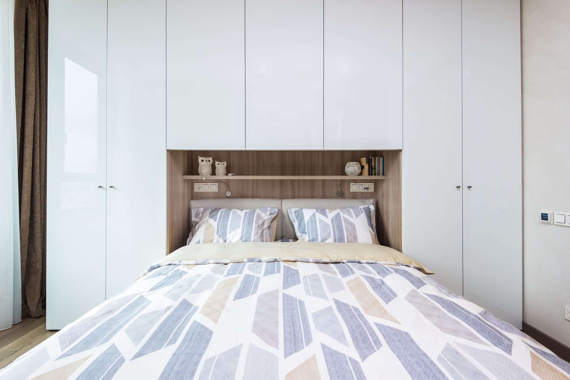 Floor-to-ceiling white flat-panel wardrobes wrapped around a bed, with a wood-lined niche and shelf over the headboard