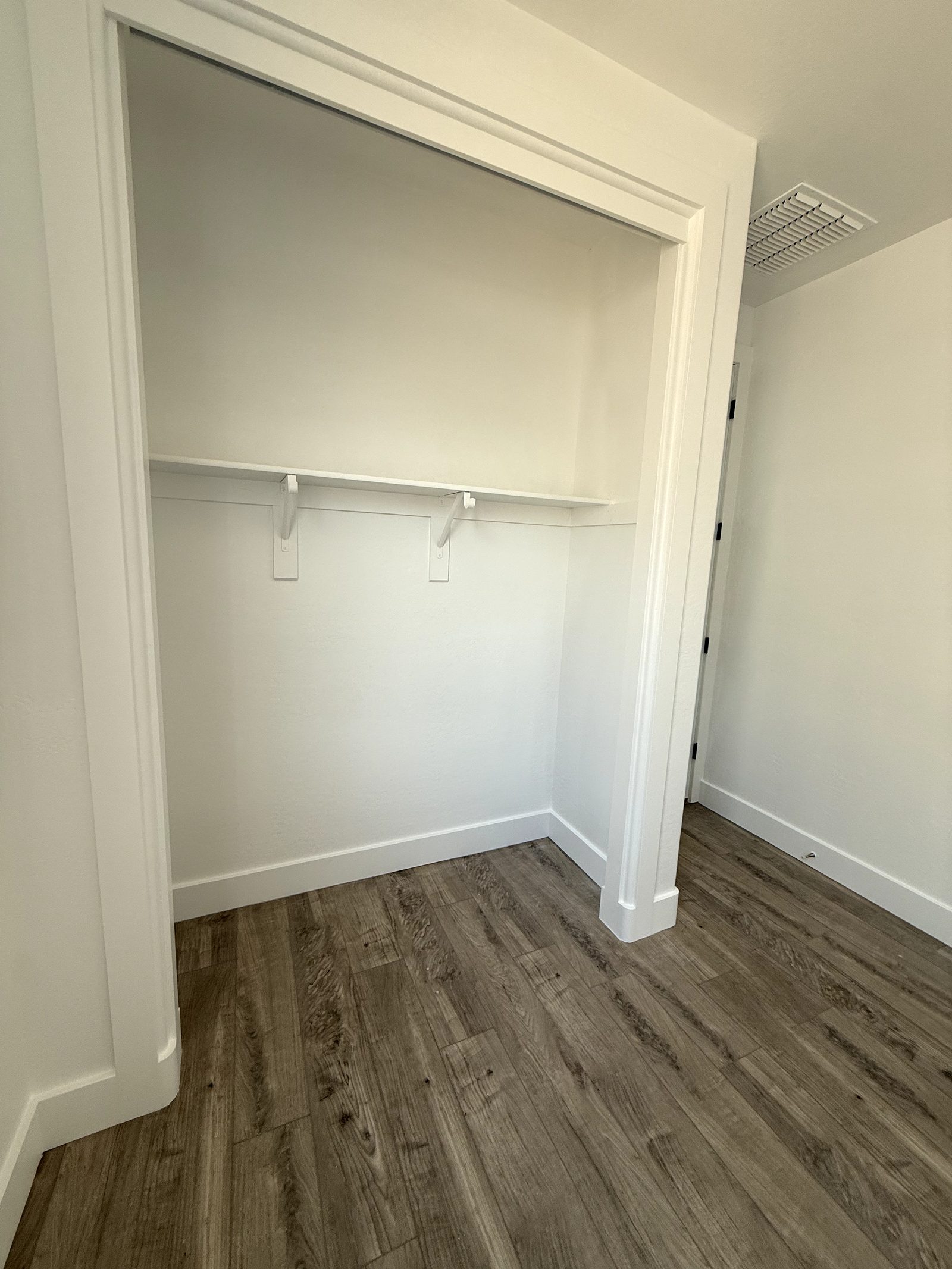 Wood look plank flooring running out of a closet opening and into a bedroom, with white baseboard scribed to the plank at the doorway