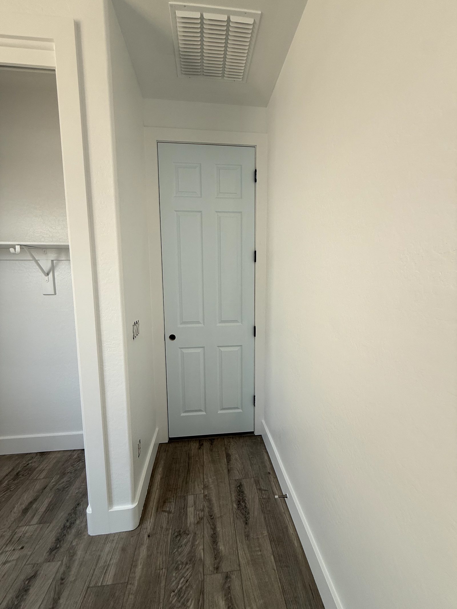 Wood look plank flooring running down a hallway to a closed door, tight to a white baseboard on both sides