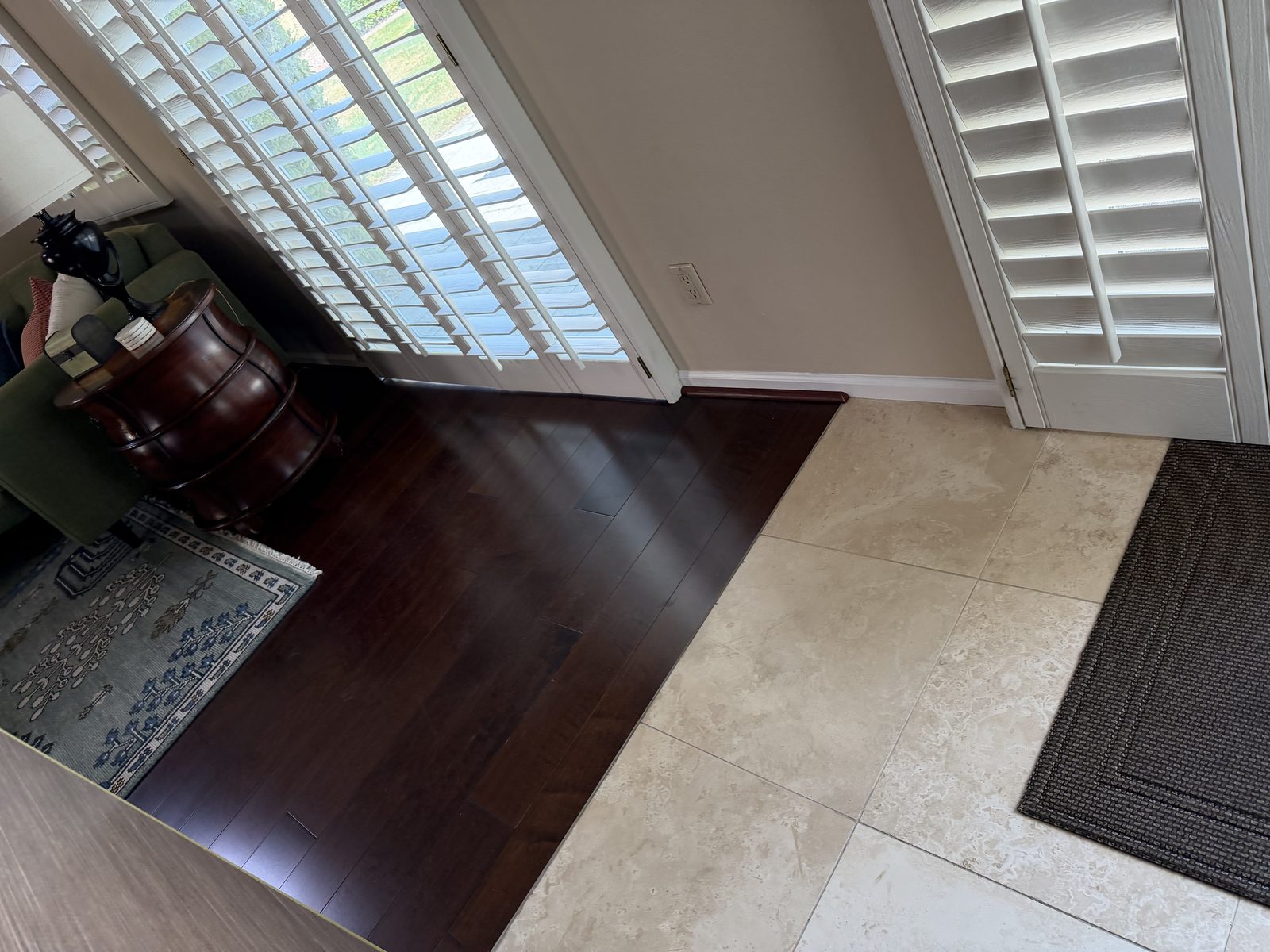 Finished transition where dark wood flooring meets travertine tile at a doorway, with repainted white baseboard running past the joint