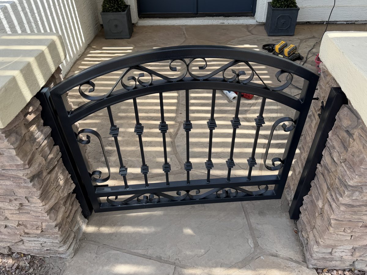 Refinished black ornamental iron courtyard gate reinstalled between stacked stone pillars in Phoenix
